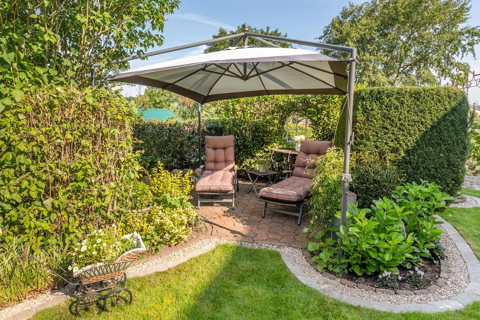 Garden with sunshade, two lounge chairs, and flower beds on stone paving.