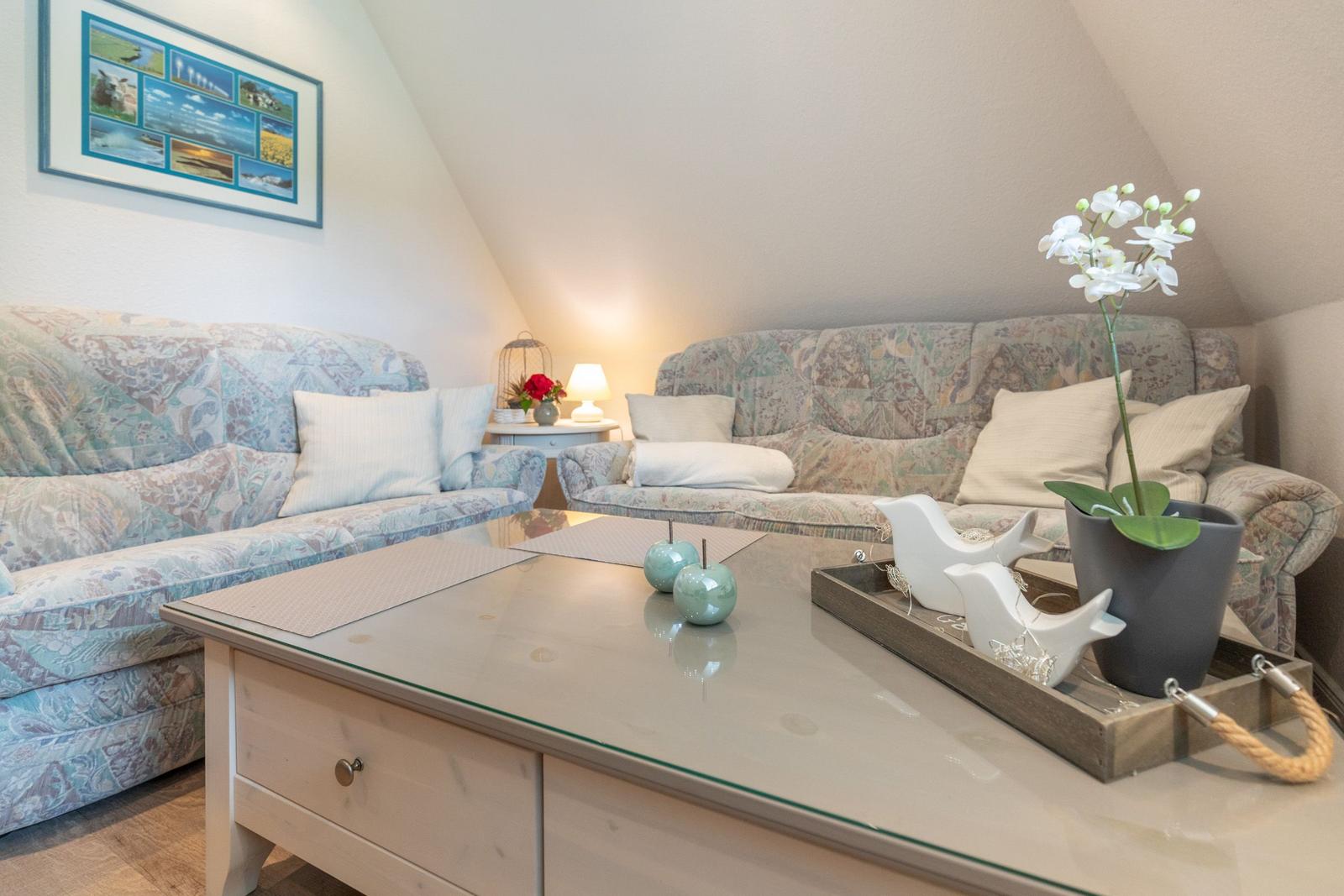 Living room with comfortable sofas, glass table, and flower decoration under sloped ceiling.