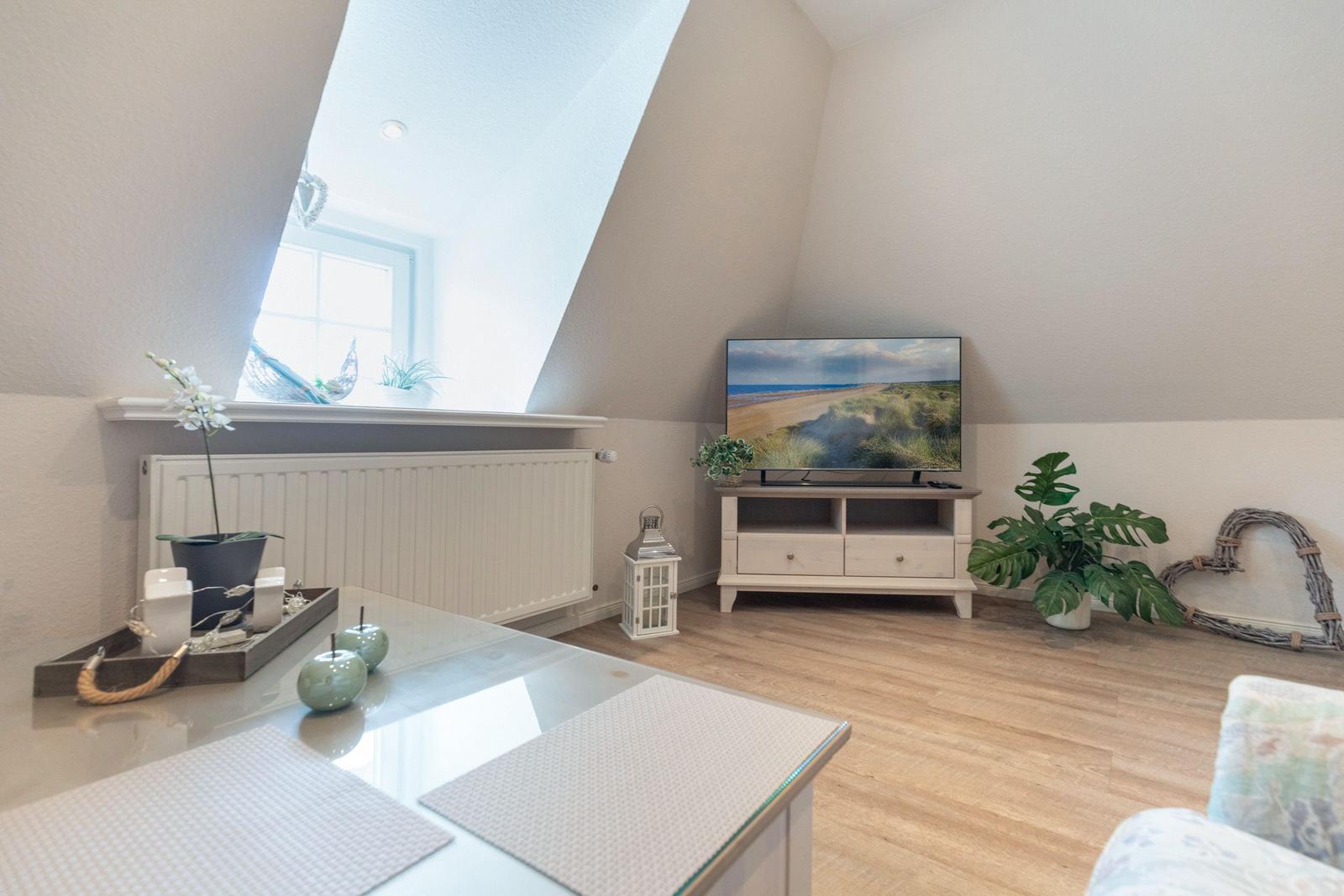 Living room with TV, plants, and skylight. Wooden floor and white cabinet.