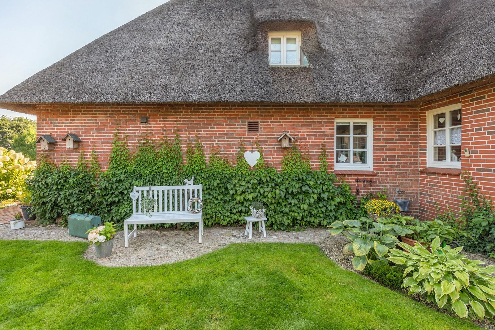 Red brick building with thatched roof, white bench, and green lawn area.