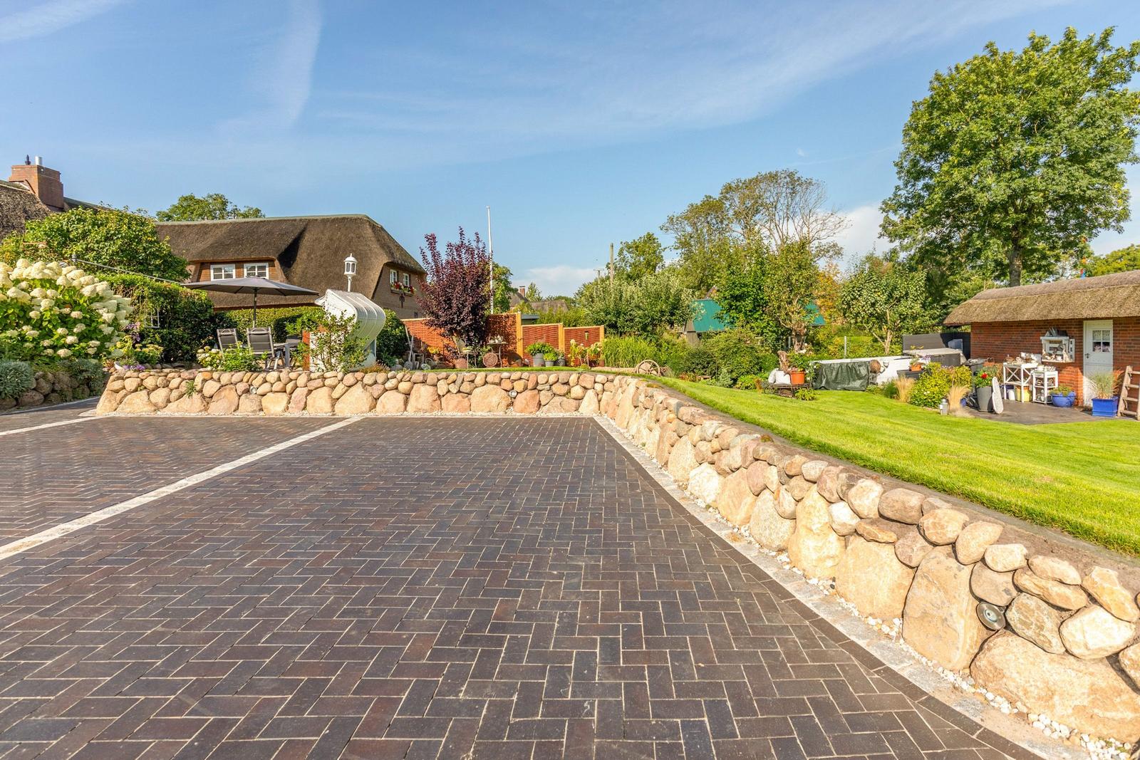 Paved courtyard with stone wall, lawn, and traditional houses with thatched roofs.