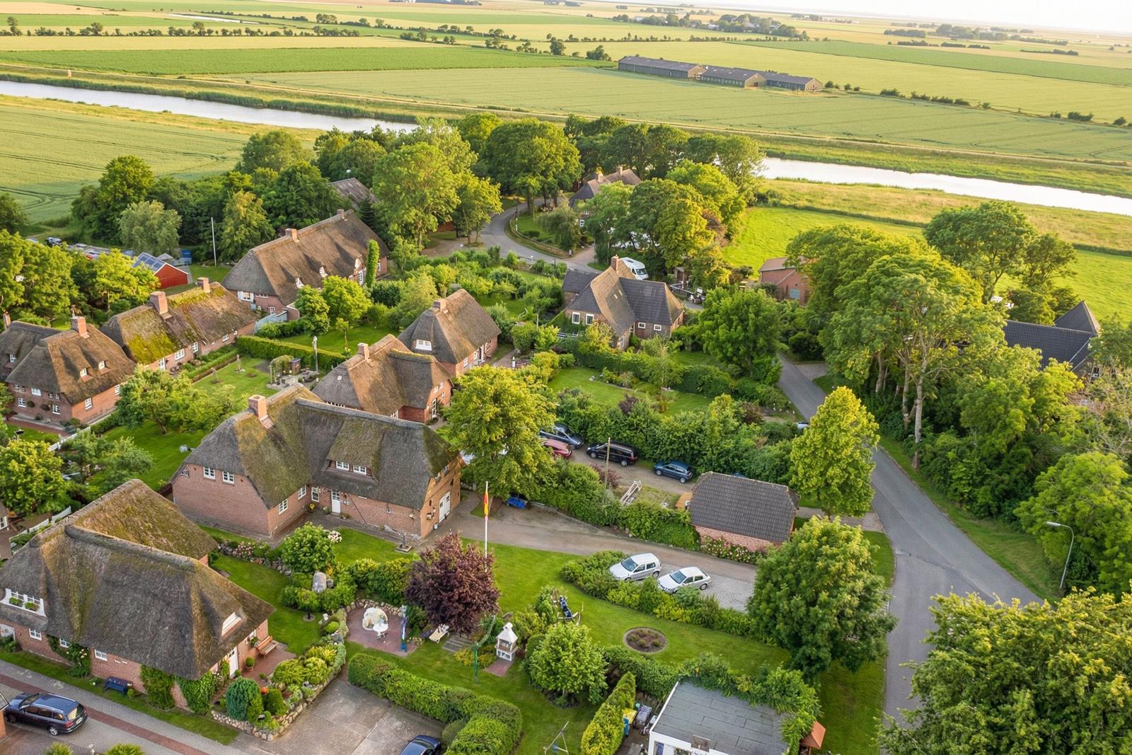 Village with thatched houses and green gardens beside a river.