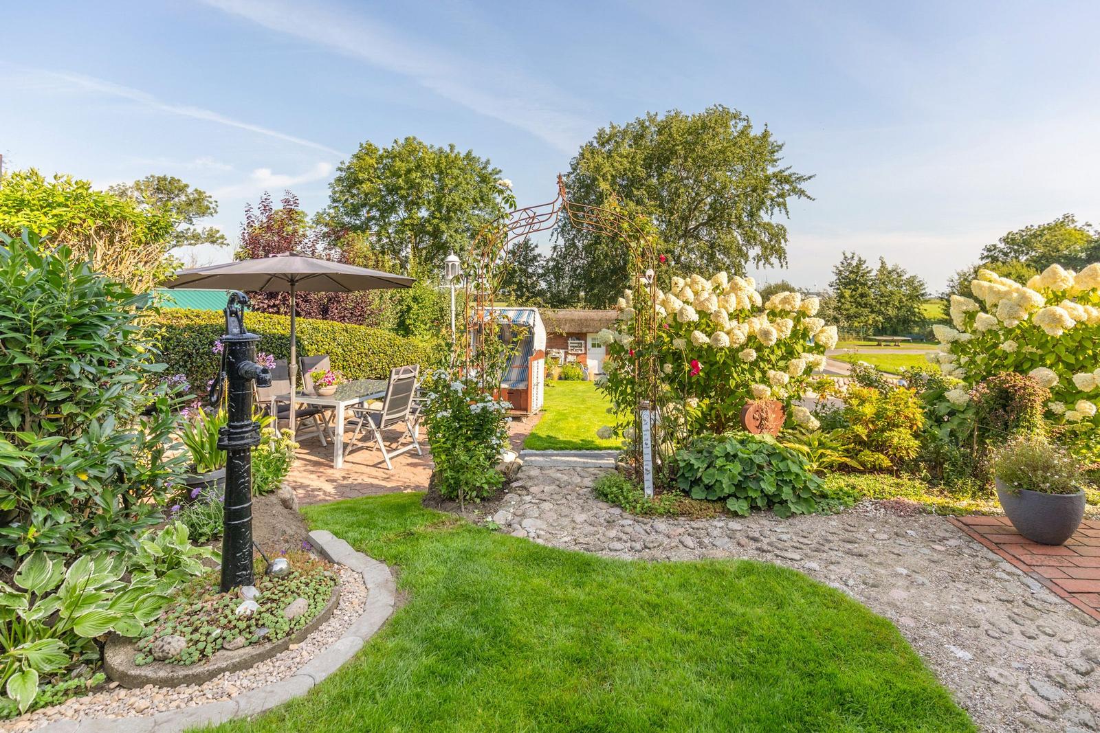 Garden with terrace, flower beds, and wrought iron arch. Cobblestone path leads to the house.