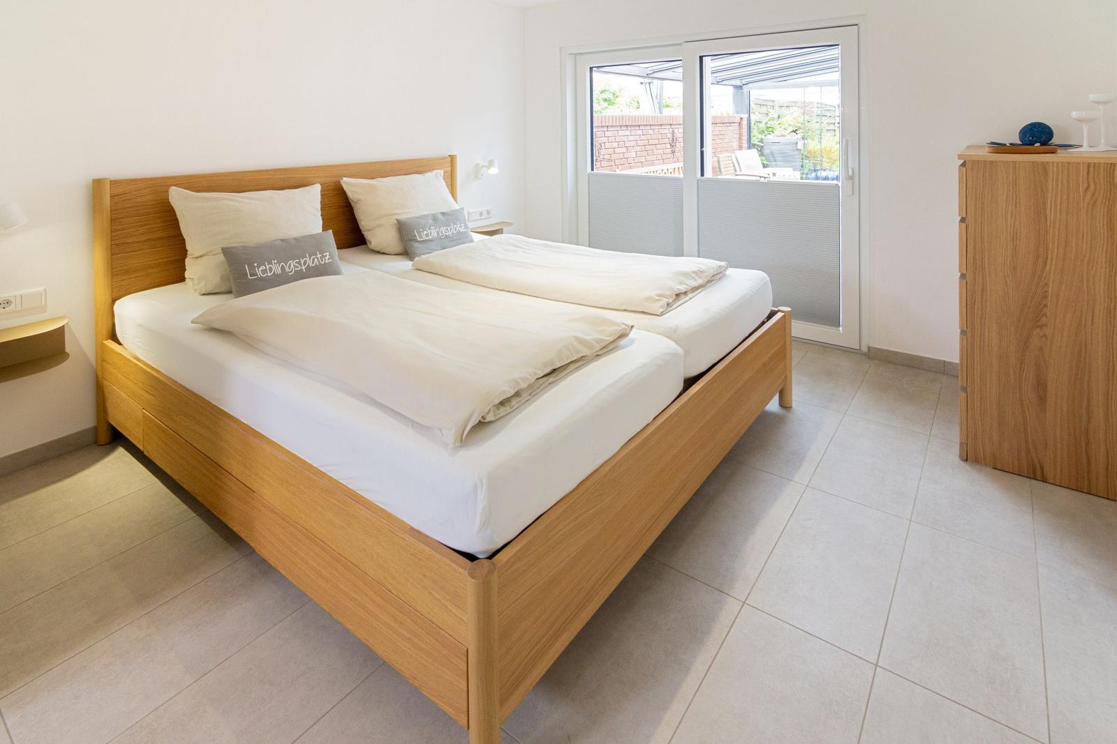 Doppelbett mit Holzrahmen, Schlafzimmer mit Glastür zum Balkon.