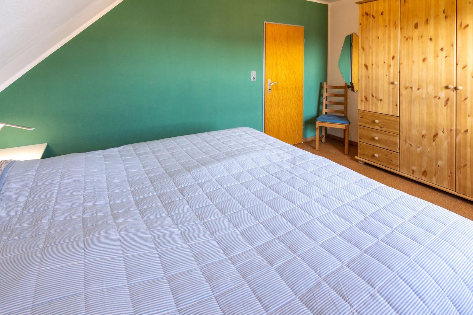 Schlafzimmer mit Bett, Kleiderschrank und Stuhl an der Wand.