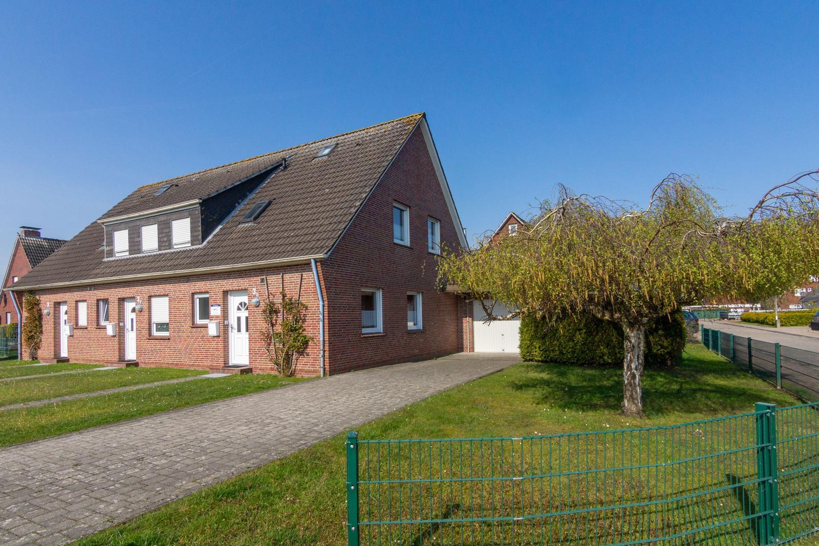Ein zweistöckiges Backsteinhaus mit Dachgauben und Vorgarten.