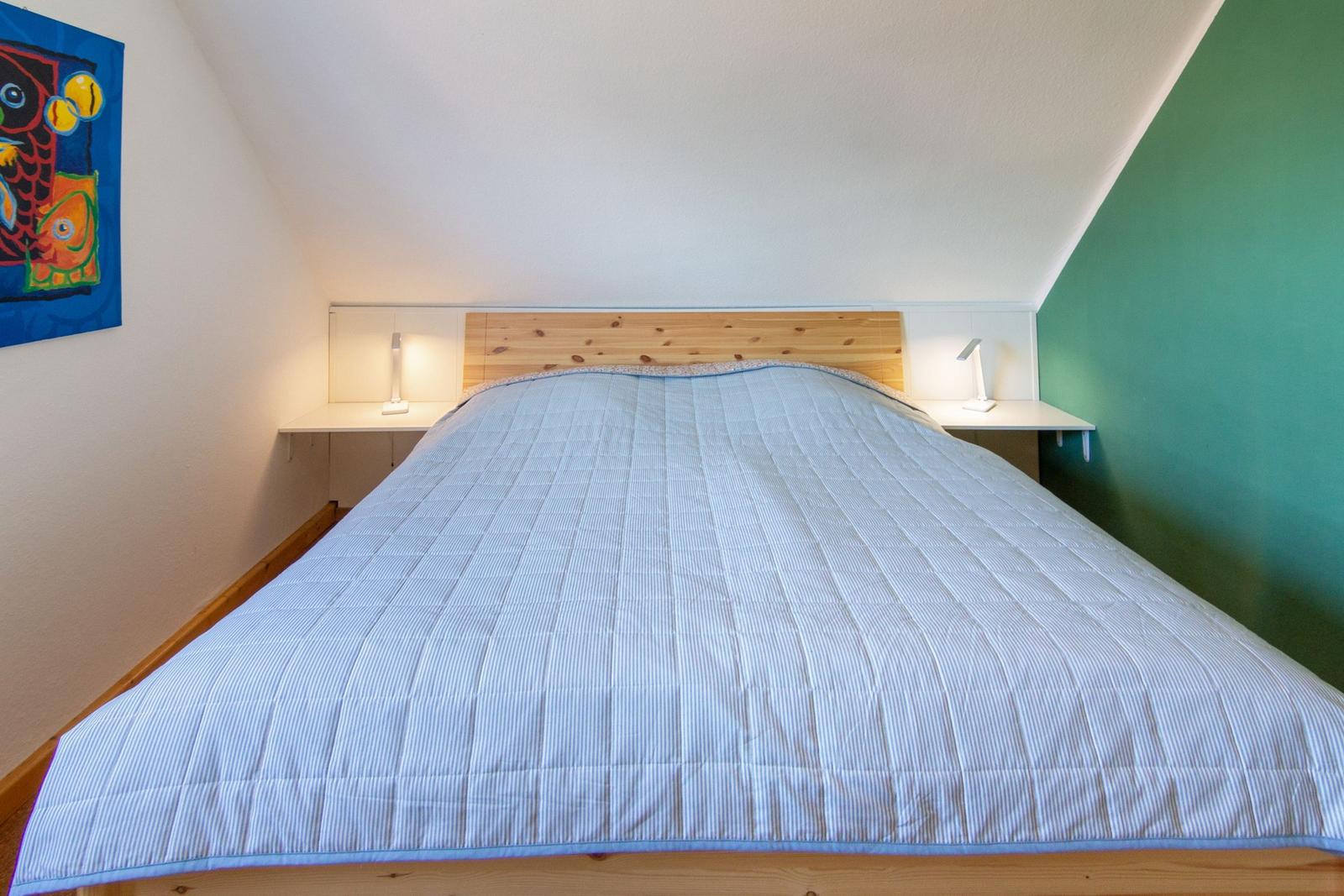 Schlafzimmer mit Doppelbett, Holzgestell und zwei Nachttischen mit Lampen.