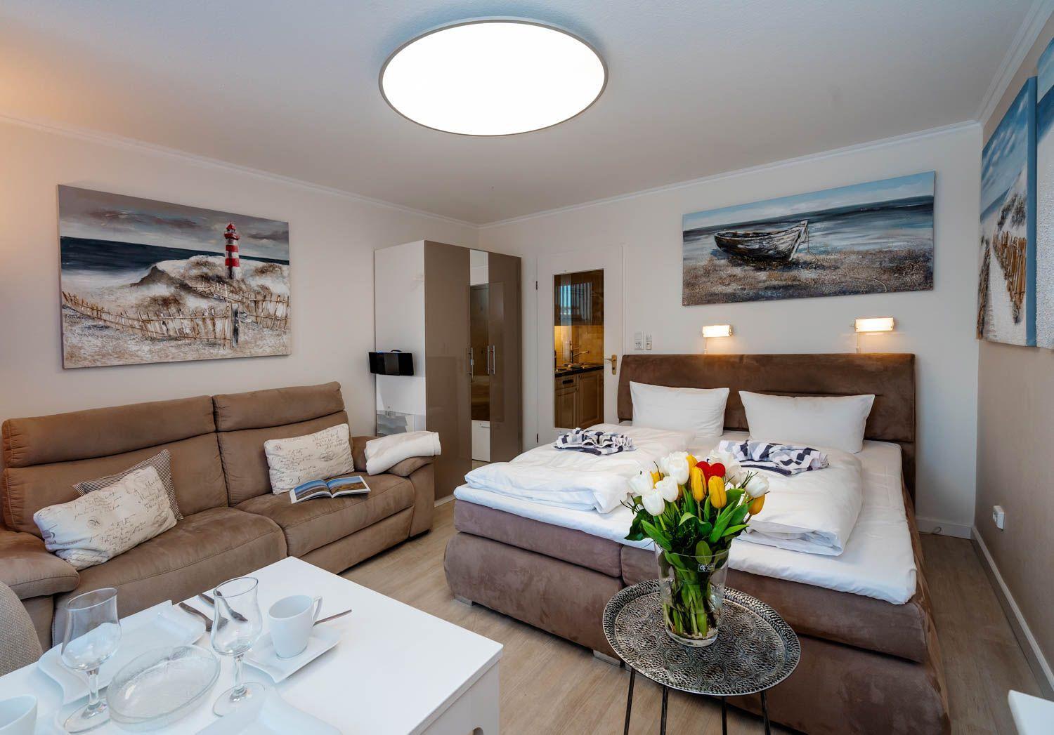 A bedroom with bed, sofa, and kitchen area. Wall paintings show beach scenes.