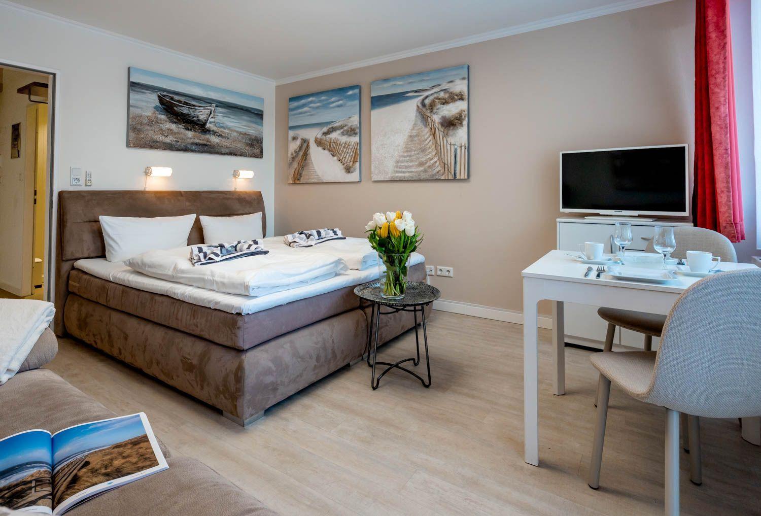Bedroom with bed, table, and TV. Wall art depicts beach landscapes.