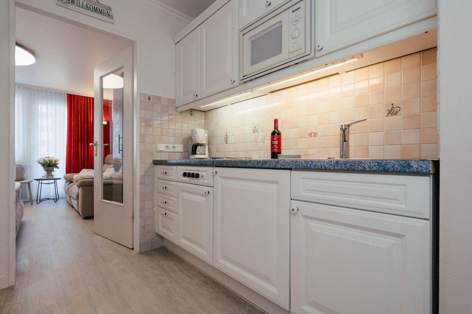 Kitchen with white cabinets, countertop, and view into living room with red curtains.