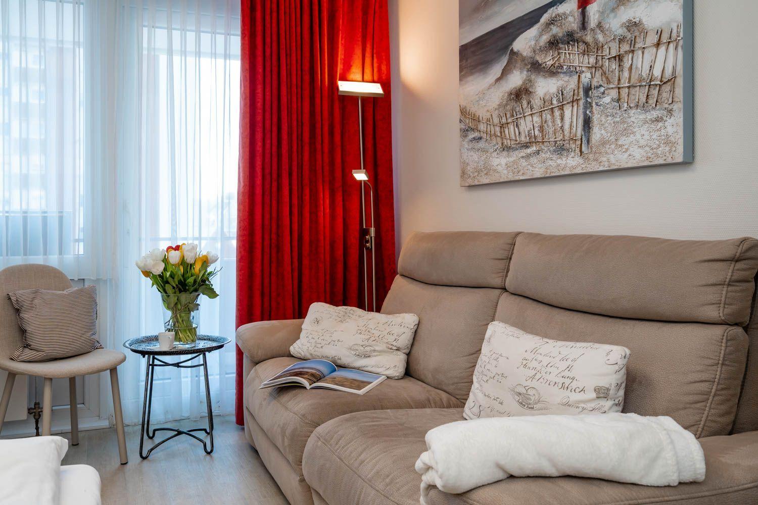 A living area with a brown sofa, red drapes, and wall decor.