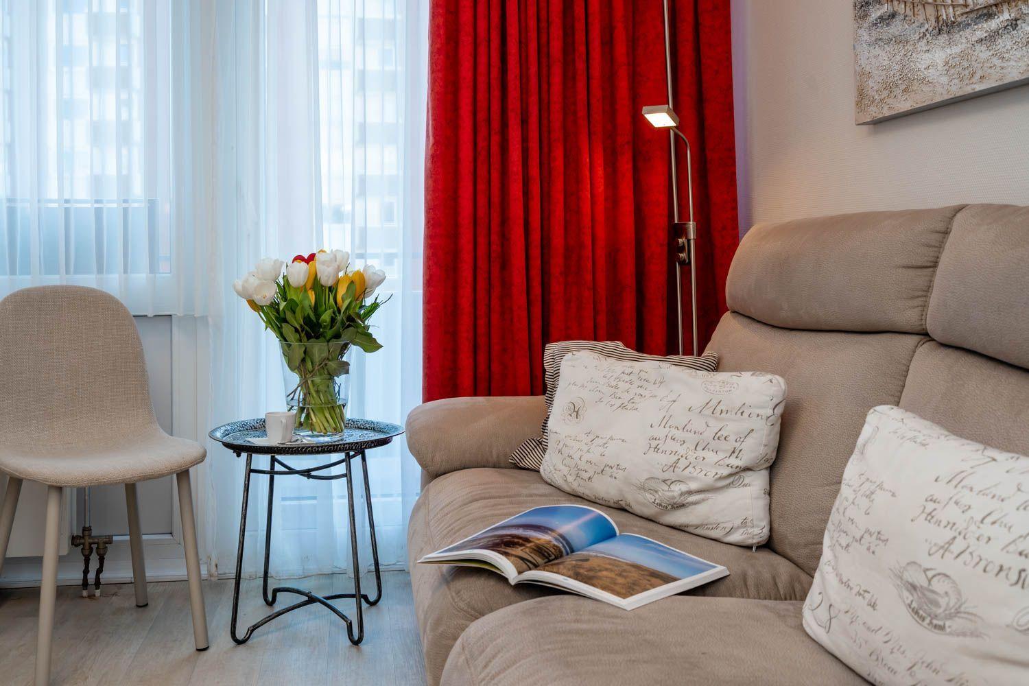 A sofa with cushions, a floor lamp, and a table with flowers and a cup.