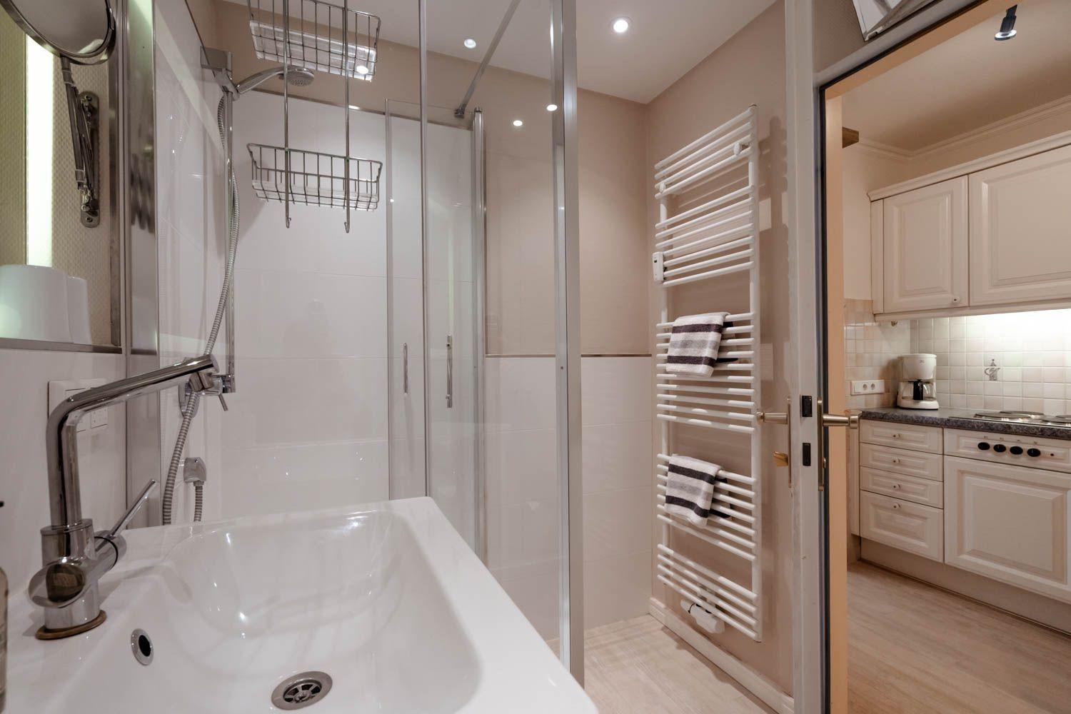 Bathroom with shower, sink, and heater. Kitchen visible in the background.