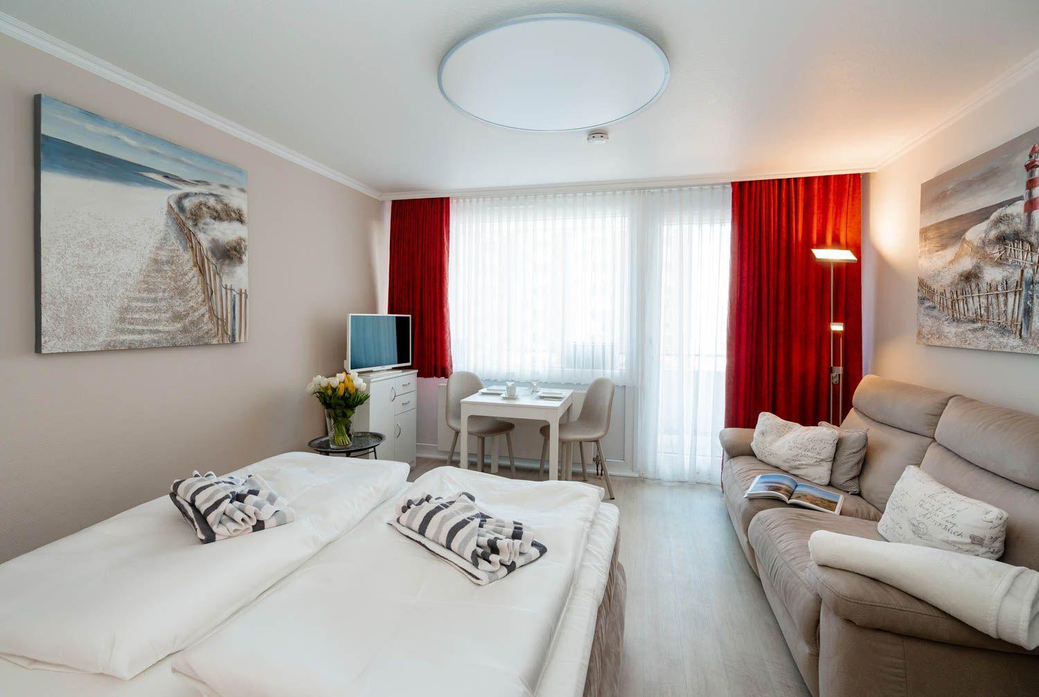 Room with sleeping area, sofa, dining table, and window with red curtains.