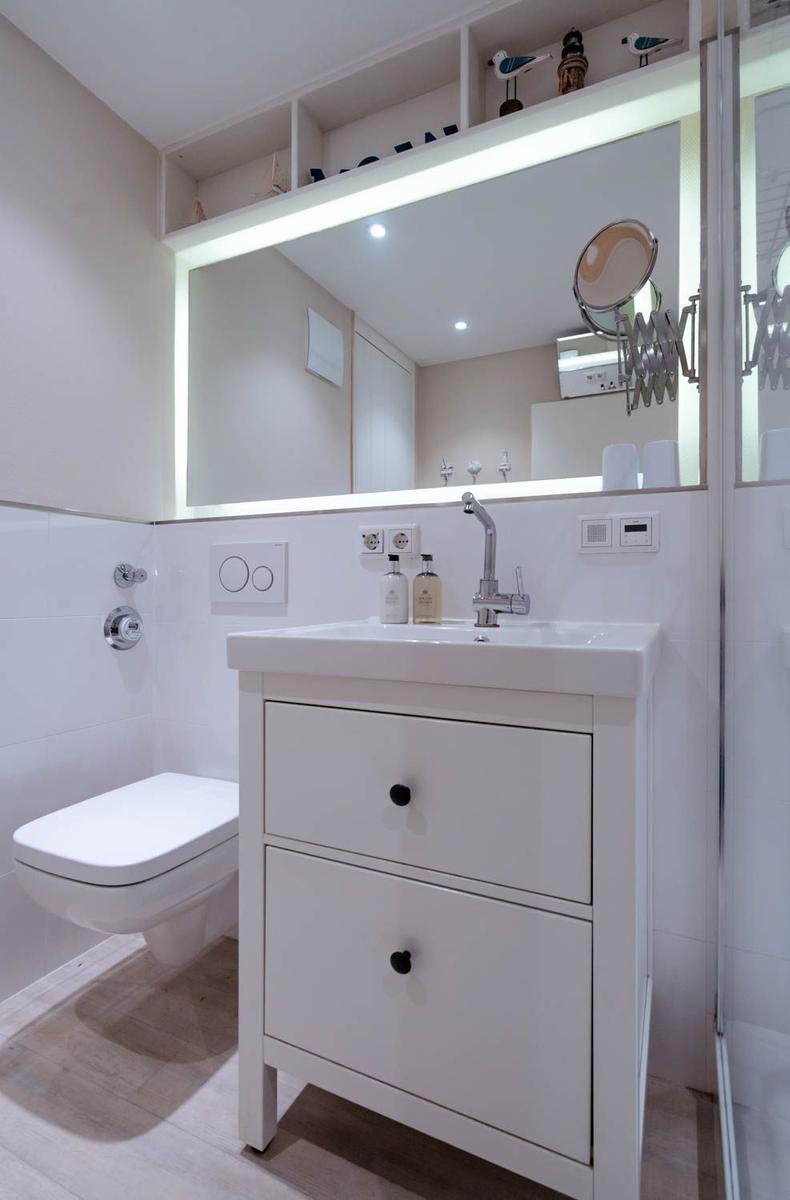 Bathroom with sink, mirror, and toilet. Shelves are above the mirror.