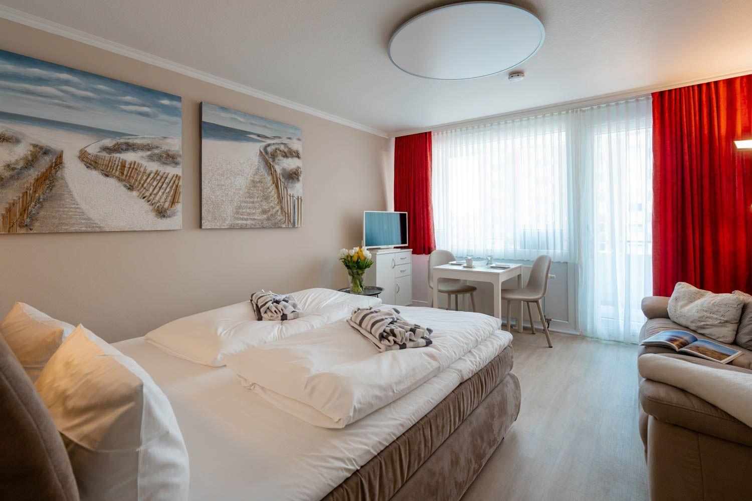 Bedroom with bed, sofa, desk, and window with red curtains.