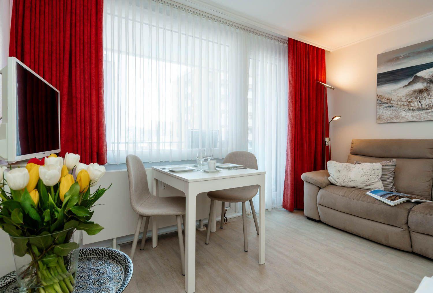 Living room with sofa, dining table, red curtains, and flowers.