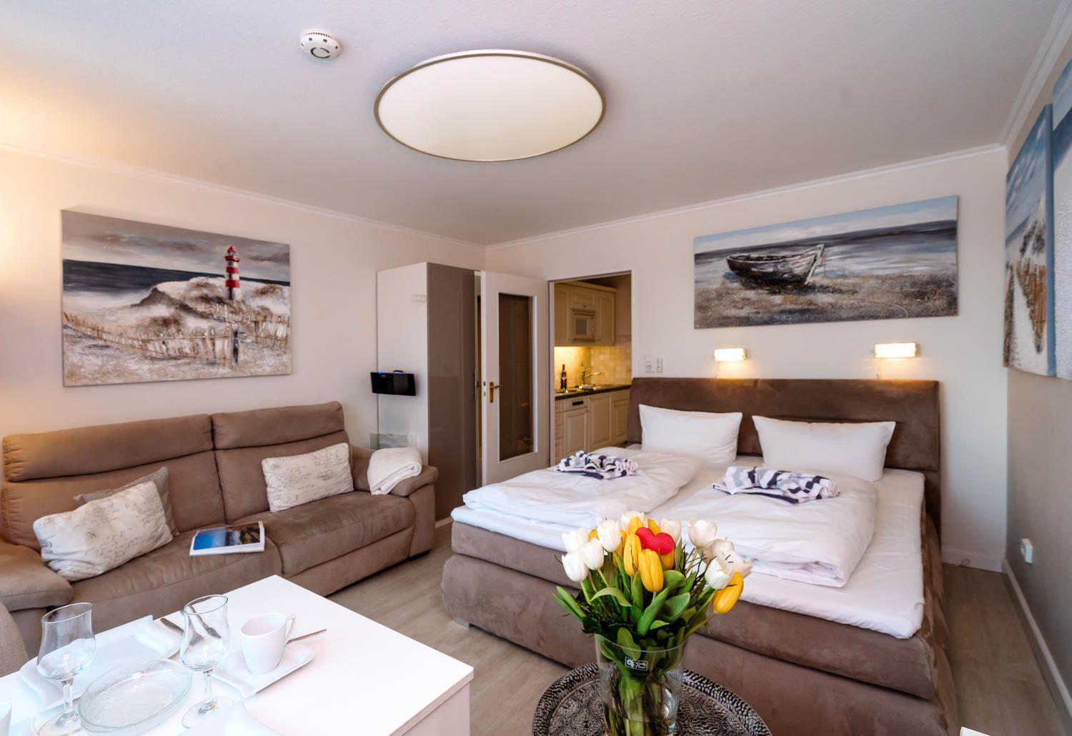 Bedroom with sofa, bed, and kitchen area. Wall paintings show coastal landscapes.