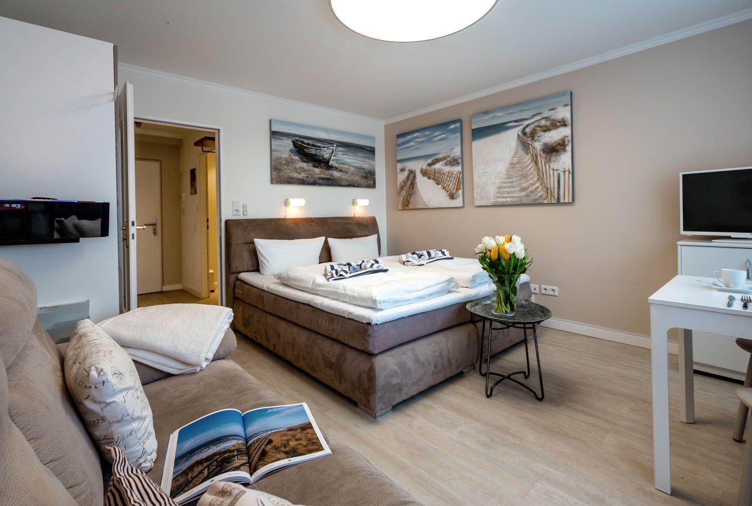 Bedroom with bed, TV, and table. Wall art shows beach landscapes.