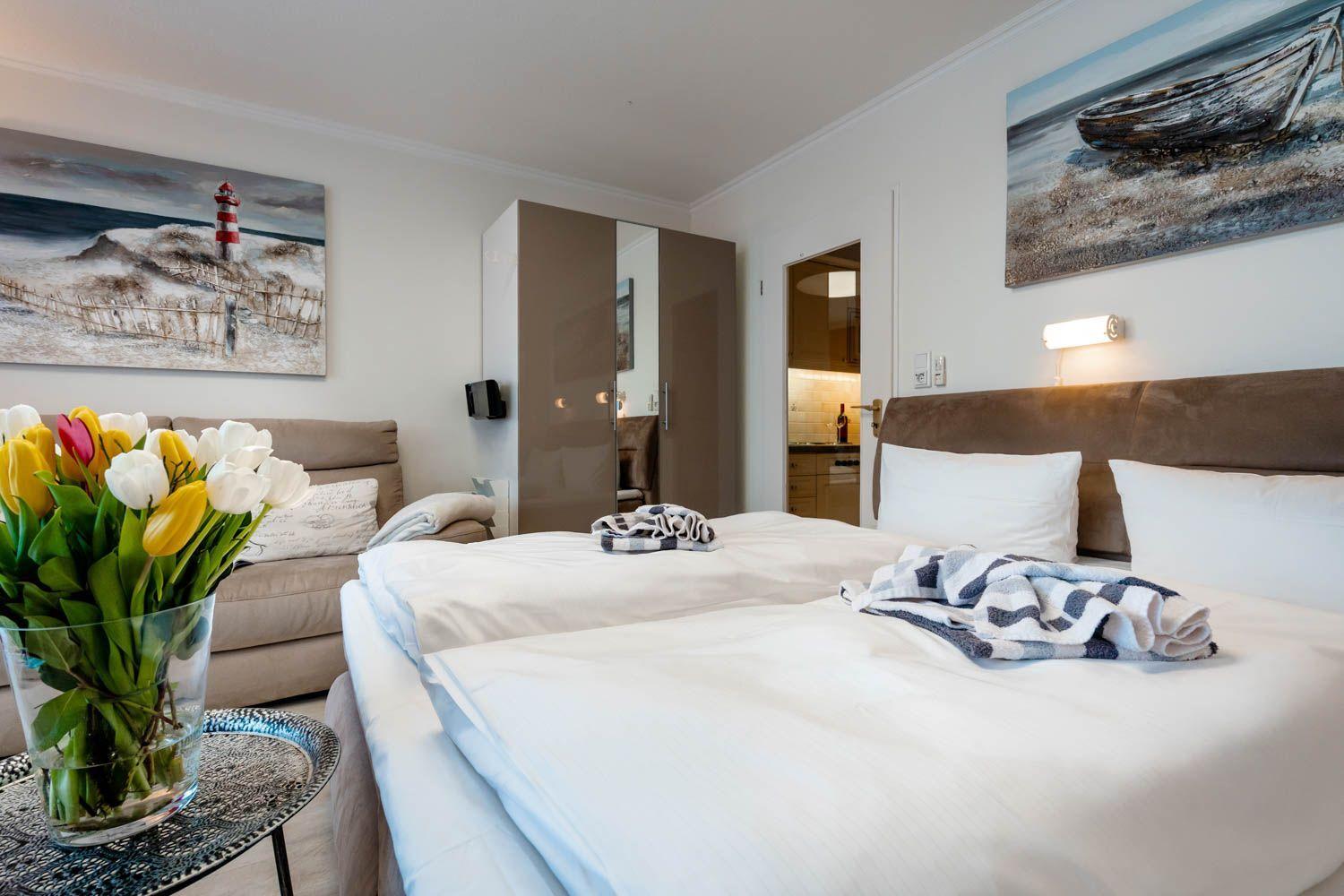 Bedroom with bed, sofa, wall art, and flowers on table.