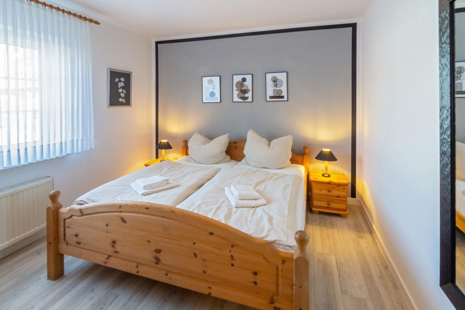 Schlafzimmer mit Holzbett, Nachttischen und Fenster mit Vorhängen.