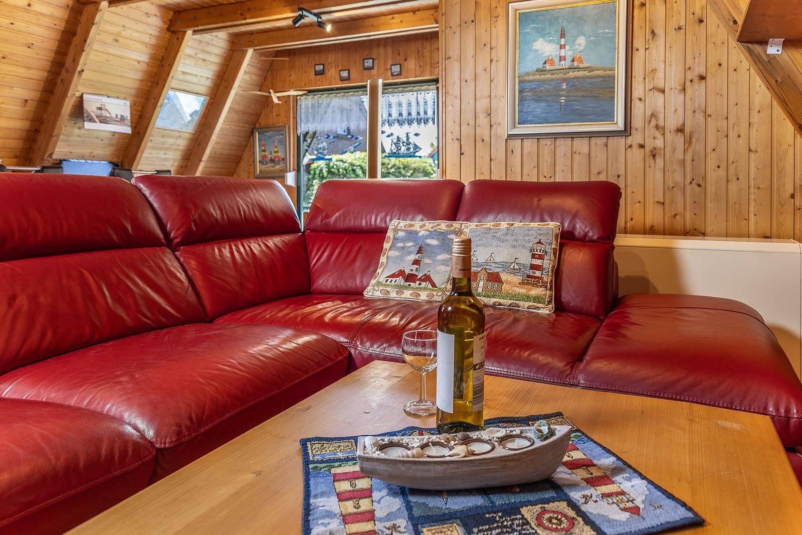 Roter Ledersofa mit Kissen und Flasche auf Holztisch in Holzhaus mit Fenster und Wandbild.