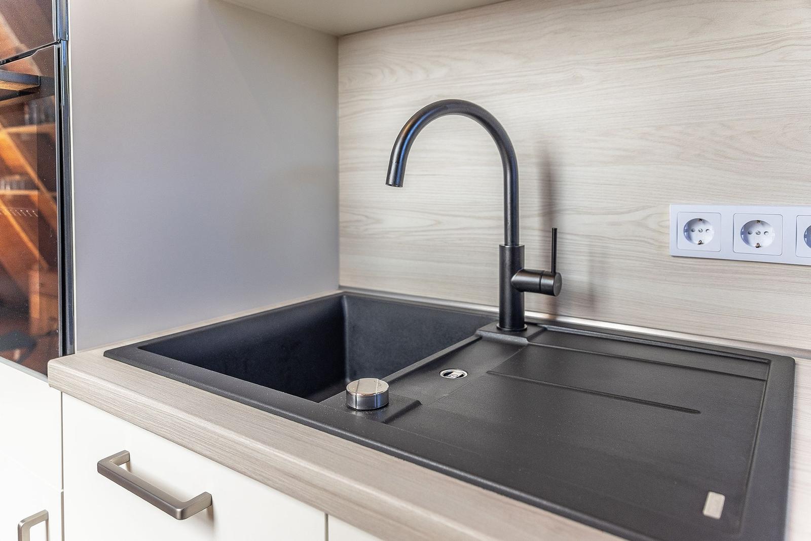 Küchenarmatur mit schwarzer Spüle und Holzoptik an der Wand.