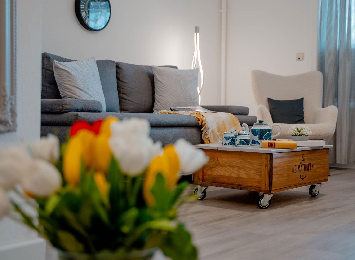 Ein Wohnzimmer mit grauem Sofa, Holztisch und Tulpen im Vordergrund.