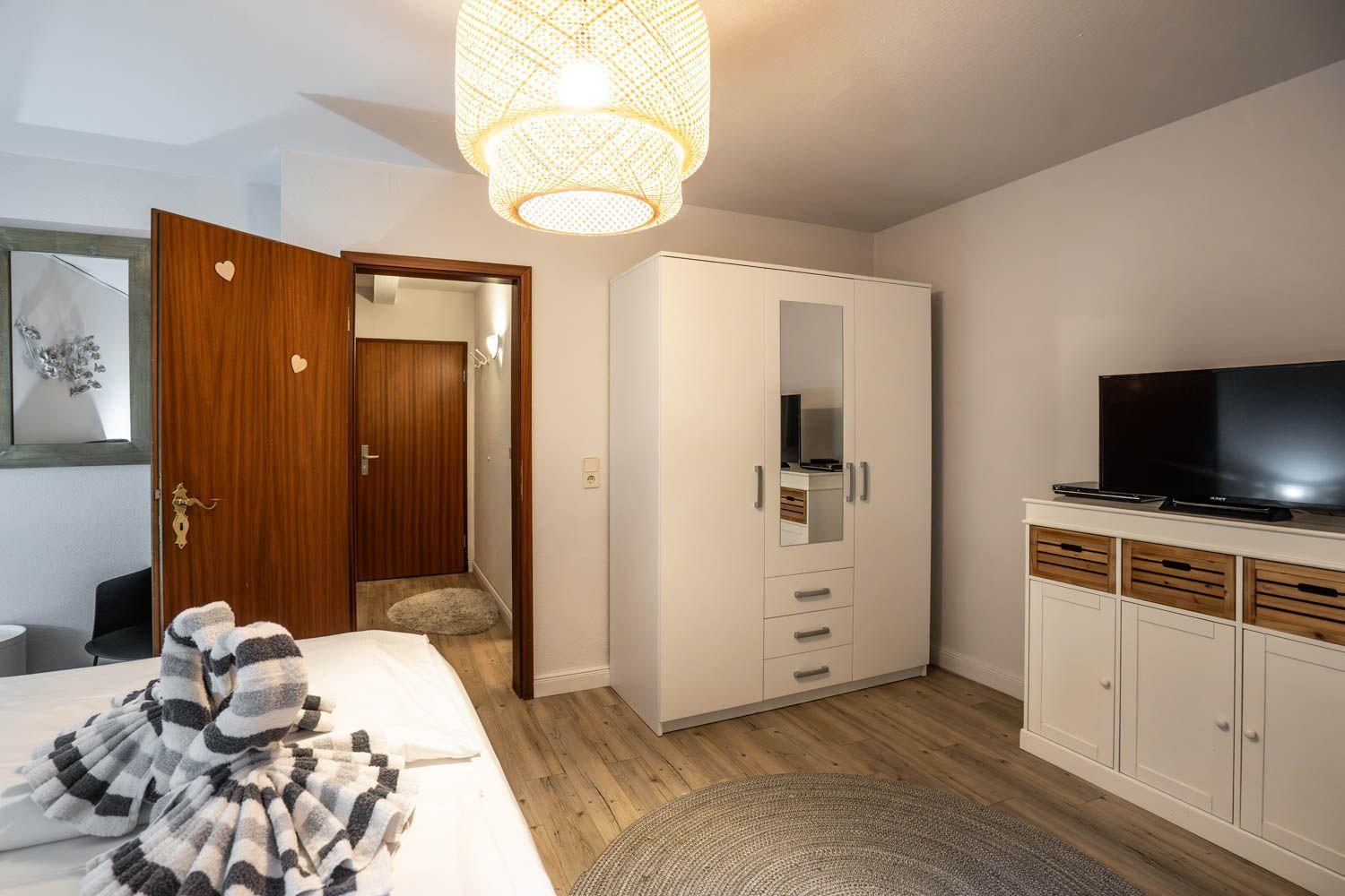 Schlafzimmer mit Bett, Kleiderschrank und Fernseher. Holzfußboden und Deckenleuchte.