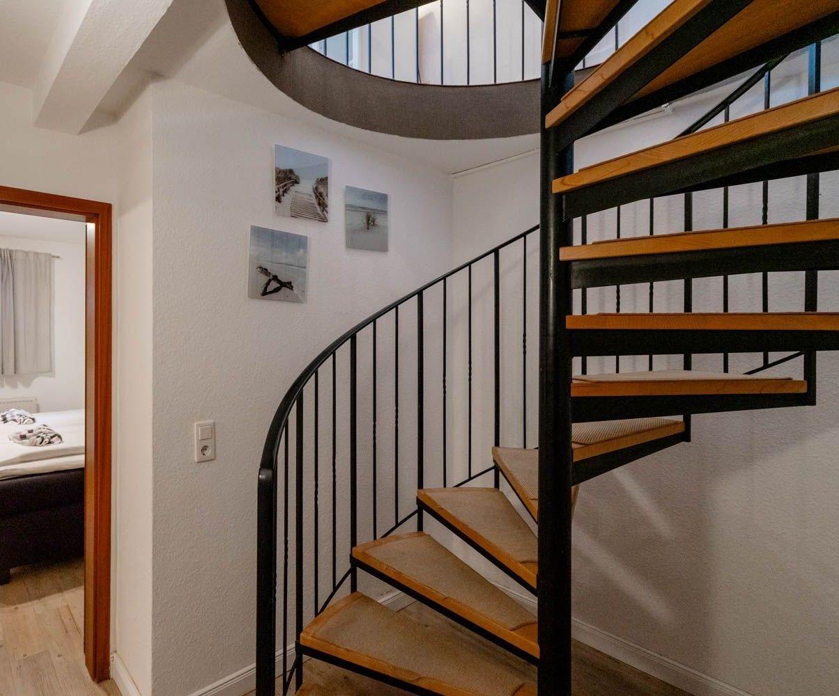 Spiralstiege mit Holzstufen und Metallgeländer führt zur oberen Etage.