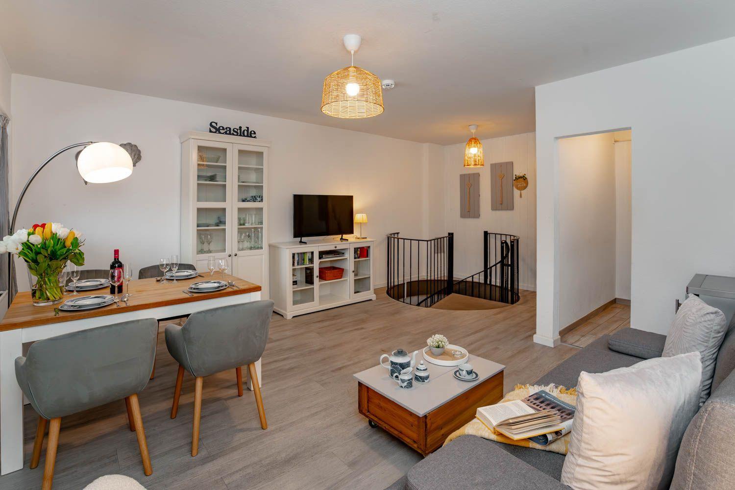 Wohn- und Essbereich mit Tisch, Sofa und TV. Hintergrund: Treppe und Schrank.
