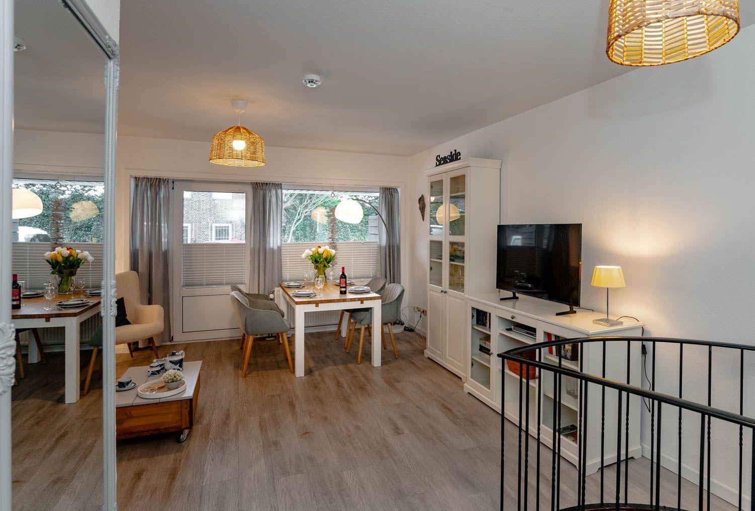 Wohn- und Essbereich mit Holzboden, TV, Schrank und Esstisch mit Stühlen.