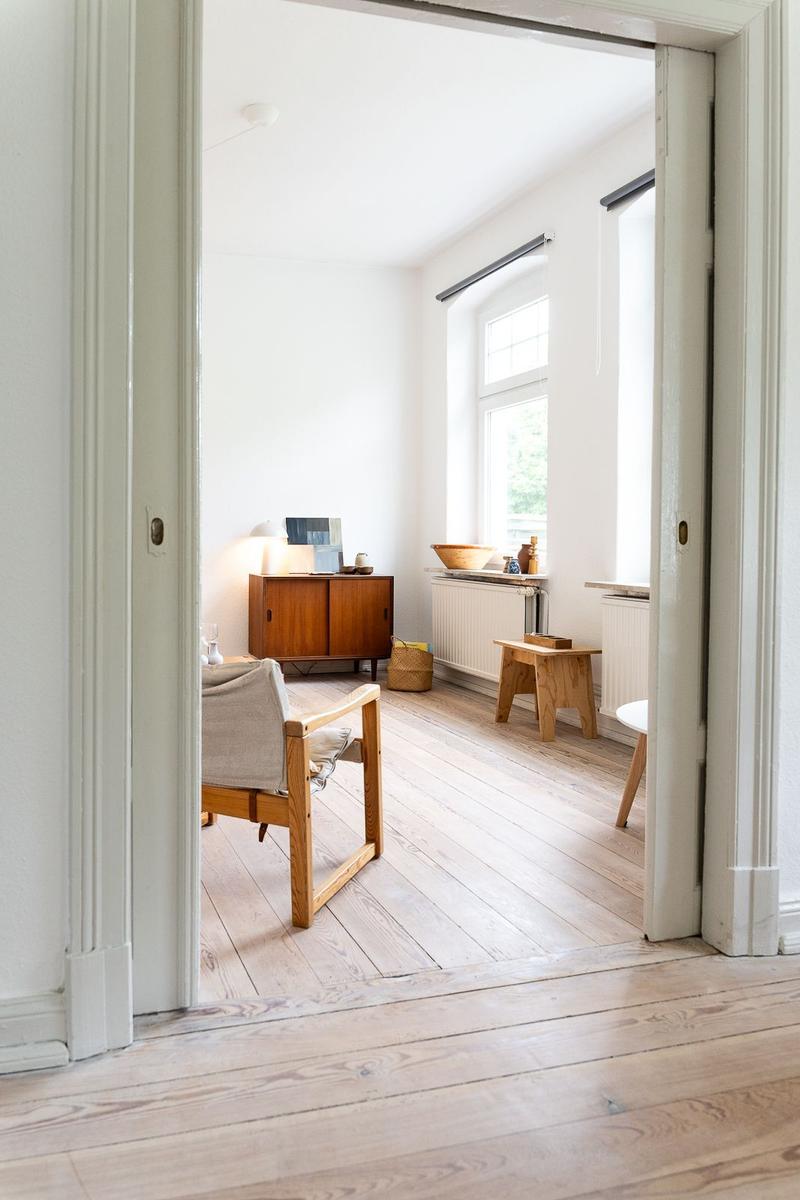 Ein Raum mit Holzboden, einem Stuhl und einem Schrank. Ein Fenster lässt Licht herein.