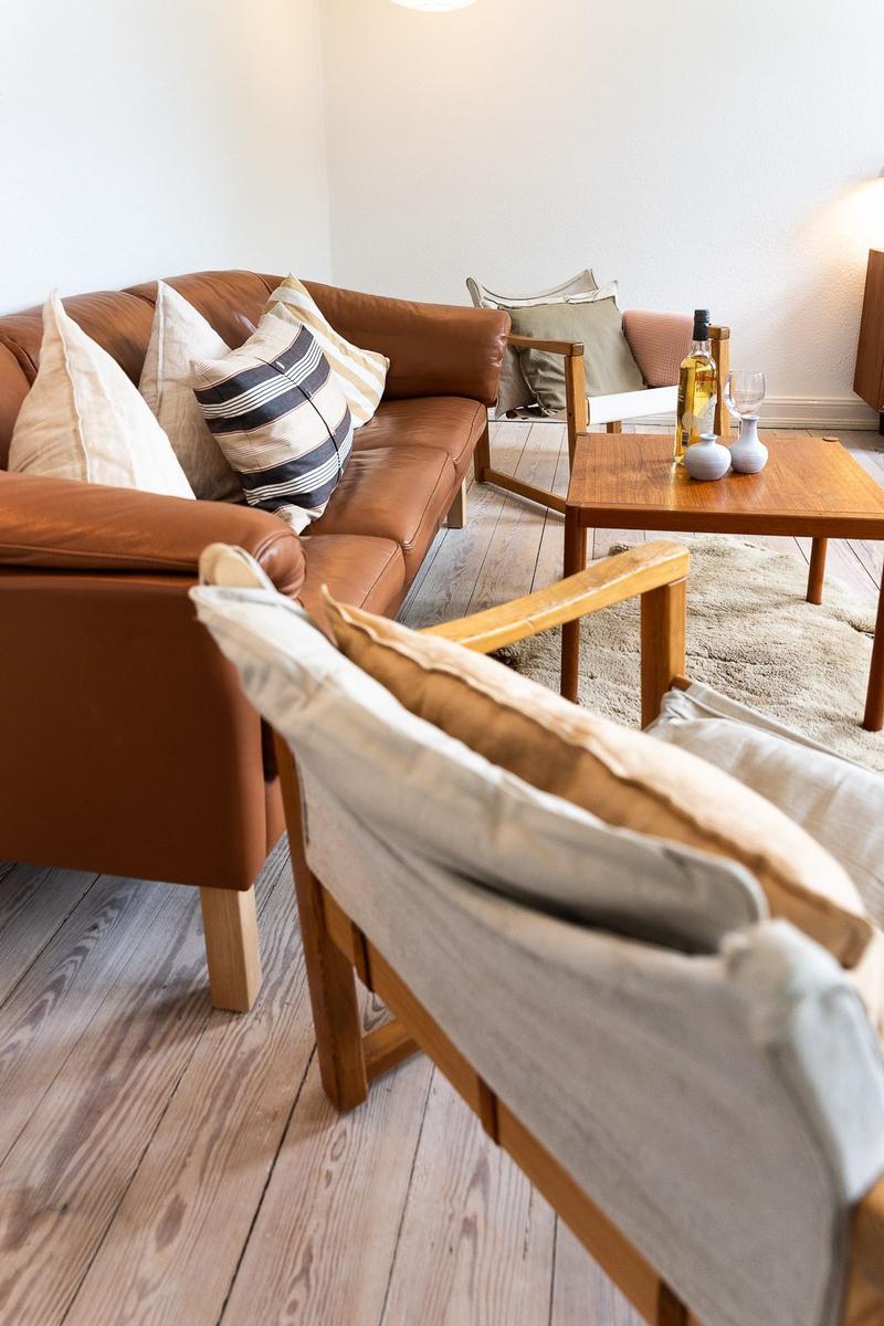 Ein Wohnzimmer mit braunem Ledersofa, Holzstühlen und einem Holztisch mit Flasche und Gläsern.