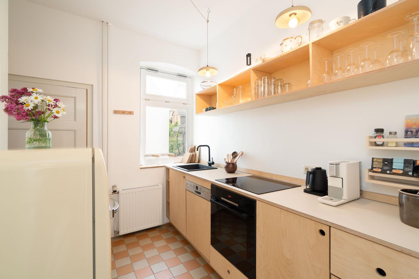 Küche mit Holzschränken, Arbeitsfläche und Fenster. Aufbewahrungshöhlen und Kühlschrank sichtbar.