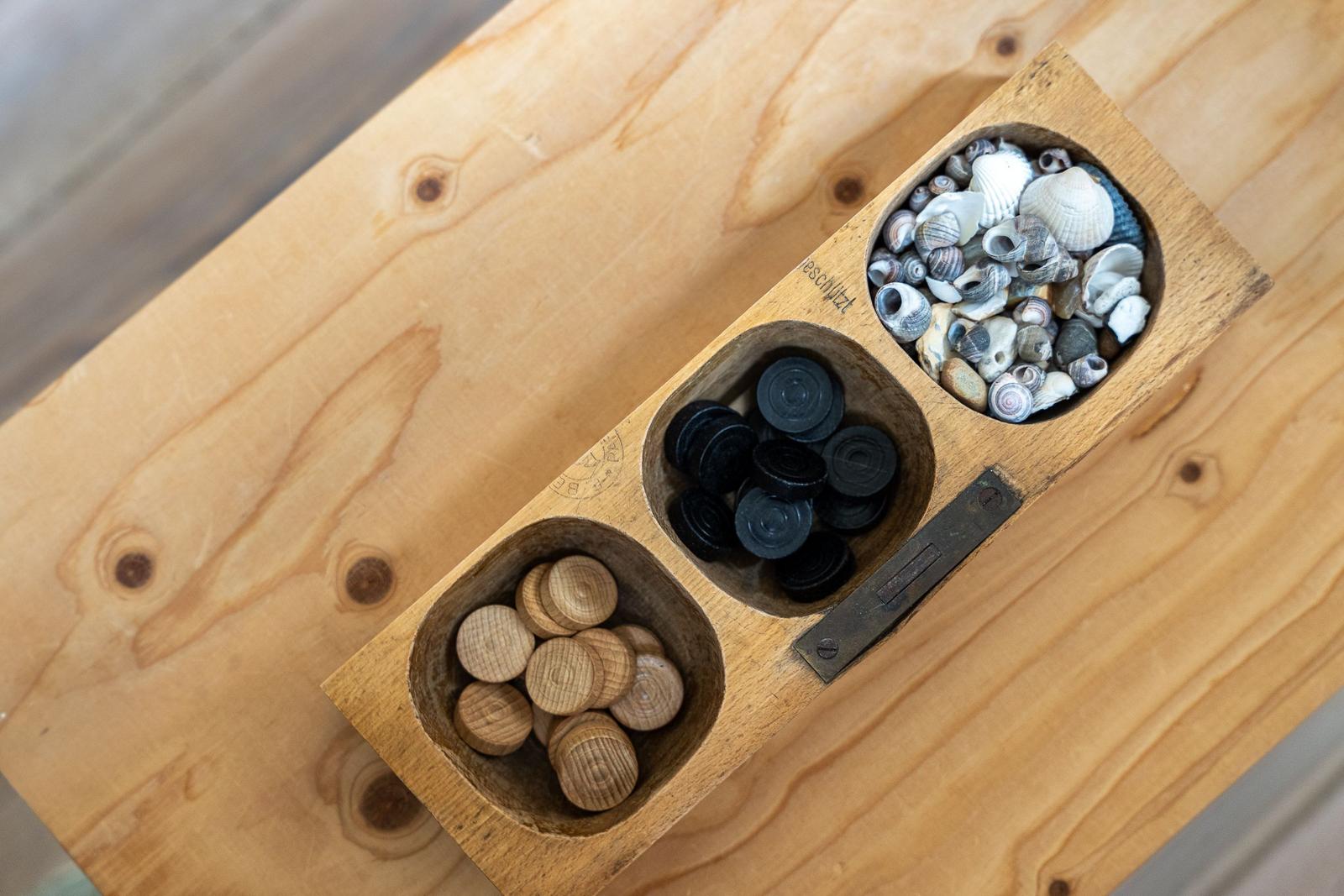 Holztablett mit drei Fächern: Muscheln, schwarzen Knöpfen und hellen Holzknöpfen auf Holztisch.