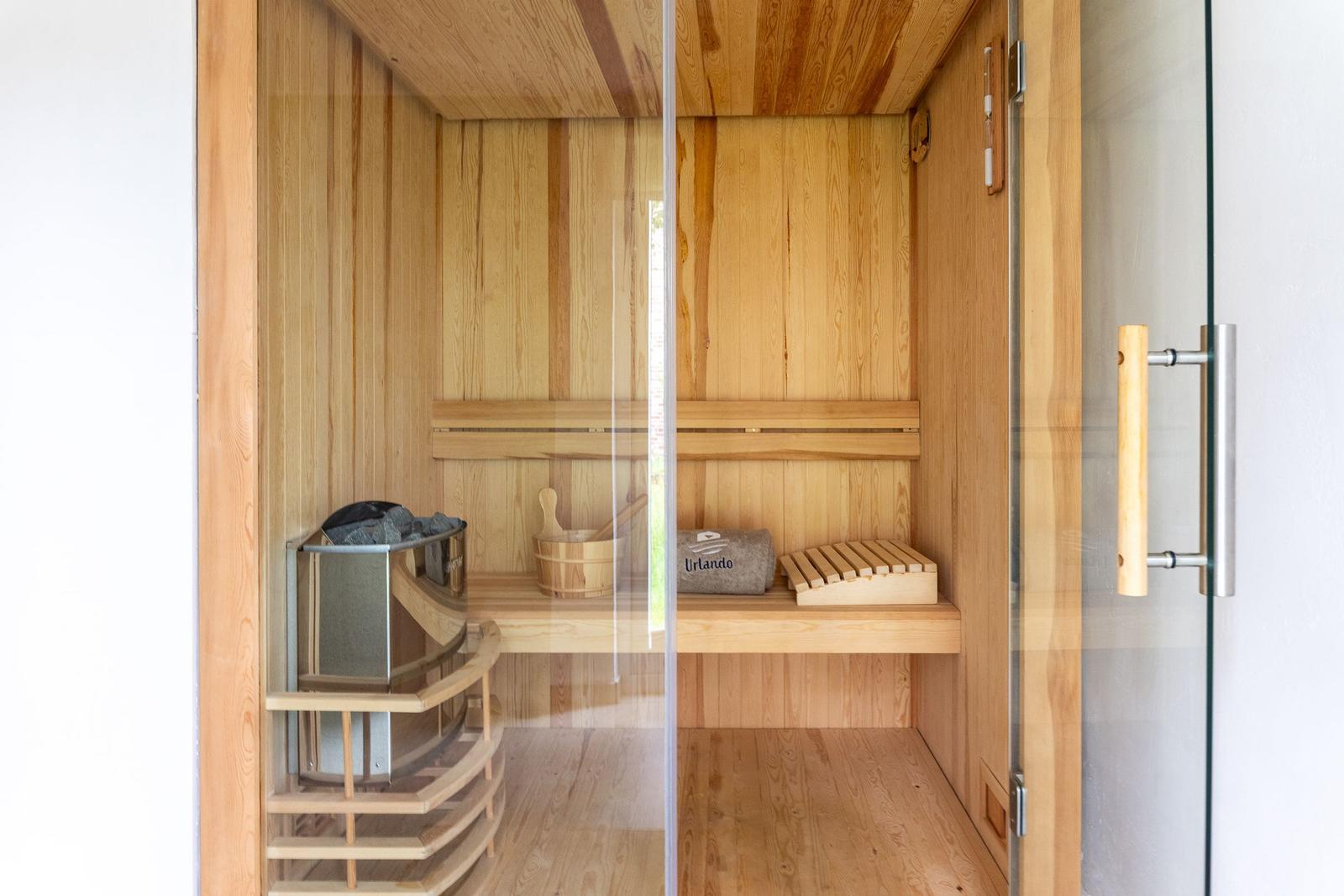 Sauna mit Holzbank, Holzstuhl und Glaswand.