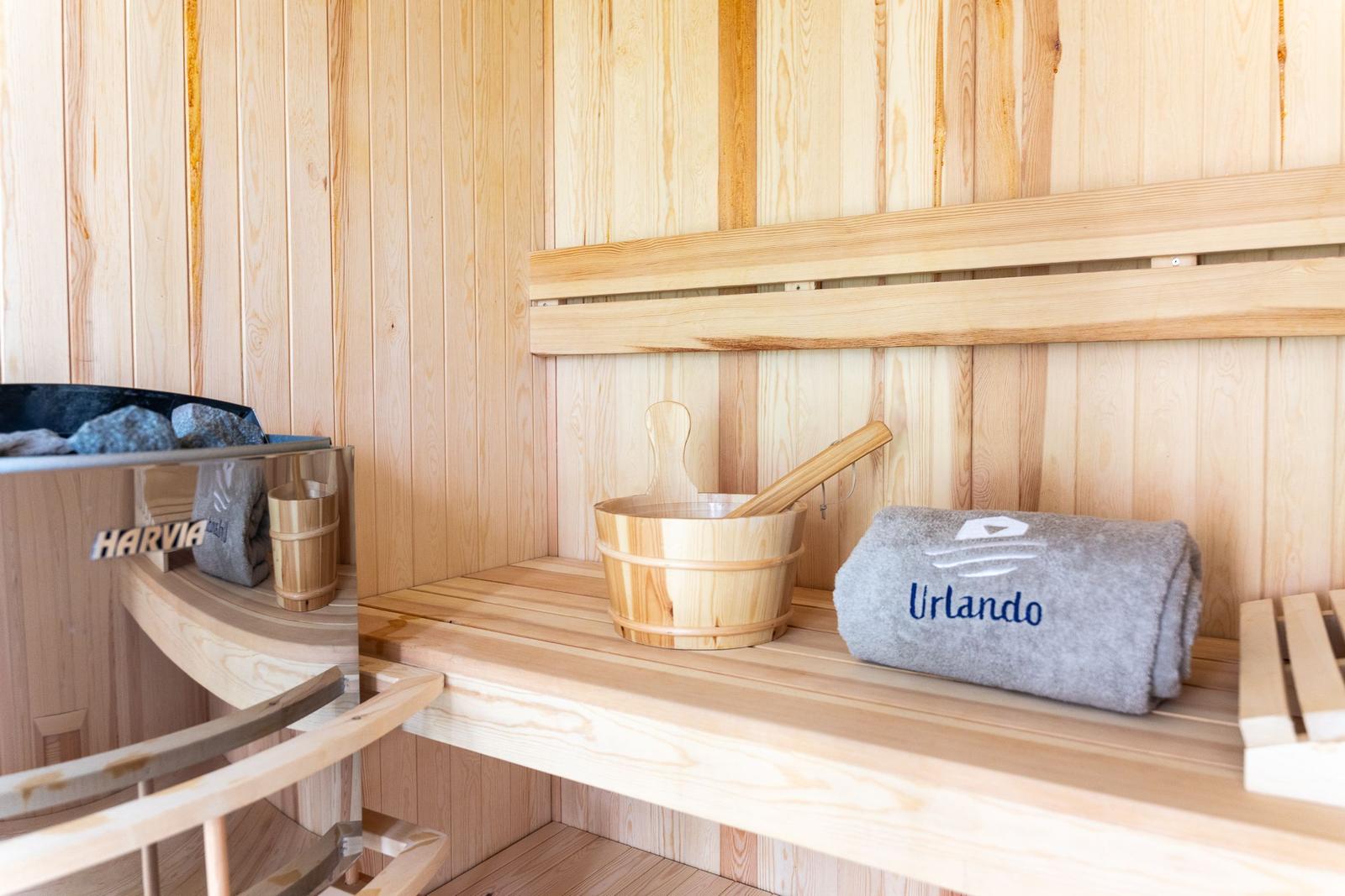 Sauna mit Holzbank, Eimer und Handtuch mit Aufschrift.