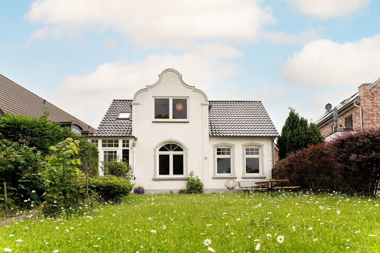 Weiße Villa mit Gartenterrasse und Blumenbeet im Vordergrund.