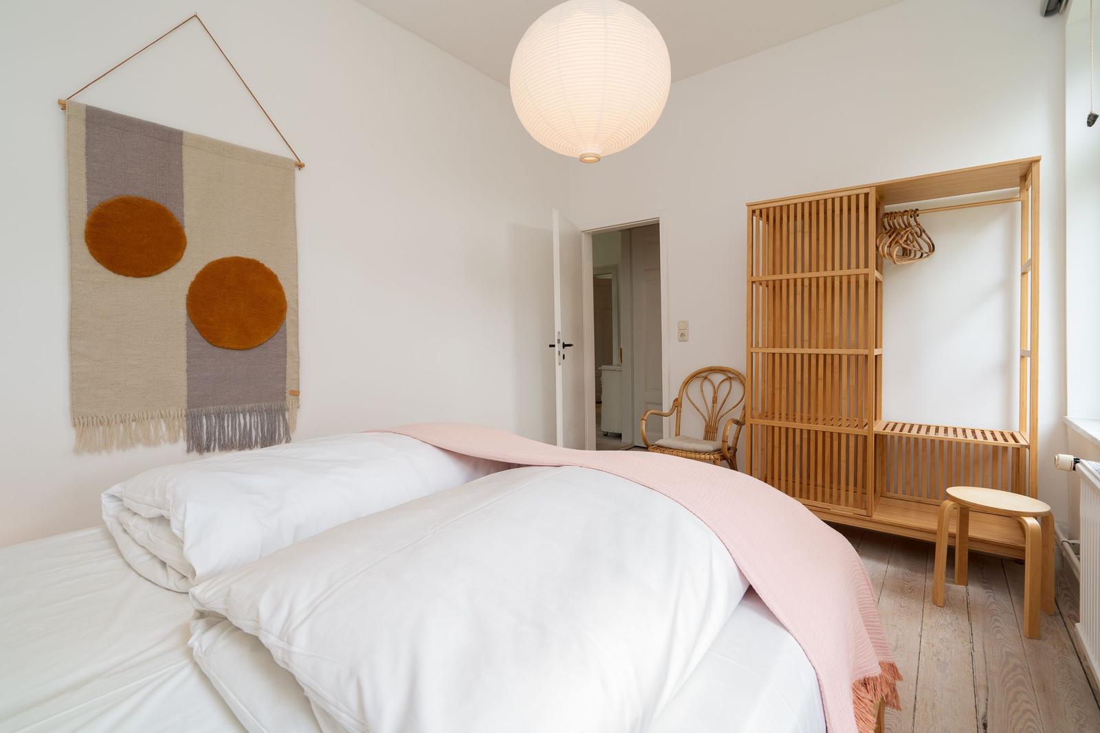 Schlafzimmer mit Bett, Holzgarderobe und Wandteppich mit runden Mustern.
