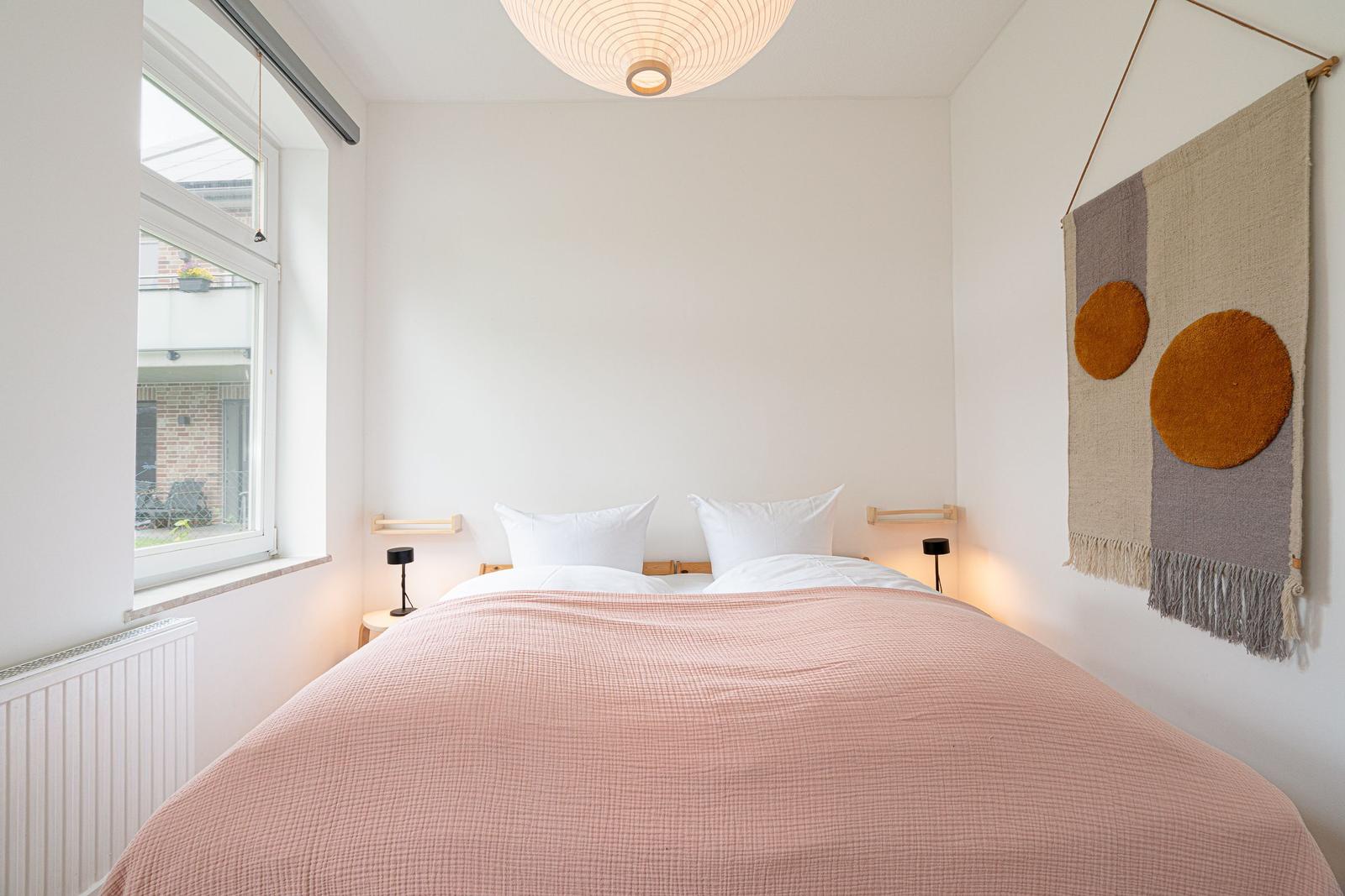 Schlafzimmer mit Bett, Fenster und Wandteppich.