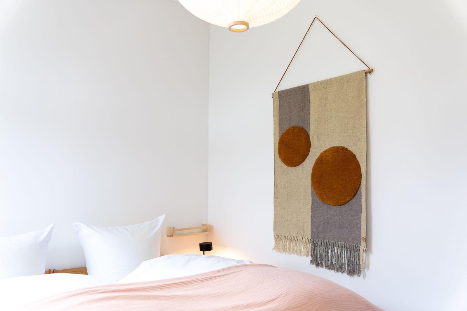 Schlafzimmer mit Bett, Wandteppich und Deckenbeleuchtung.