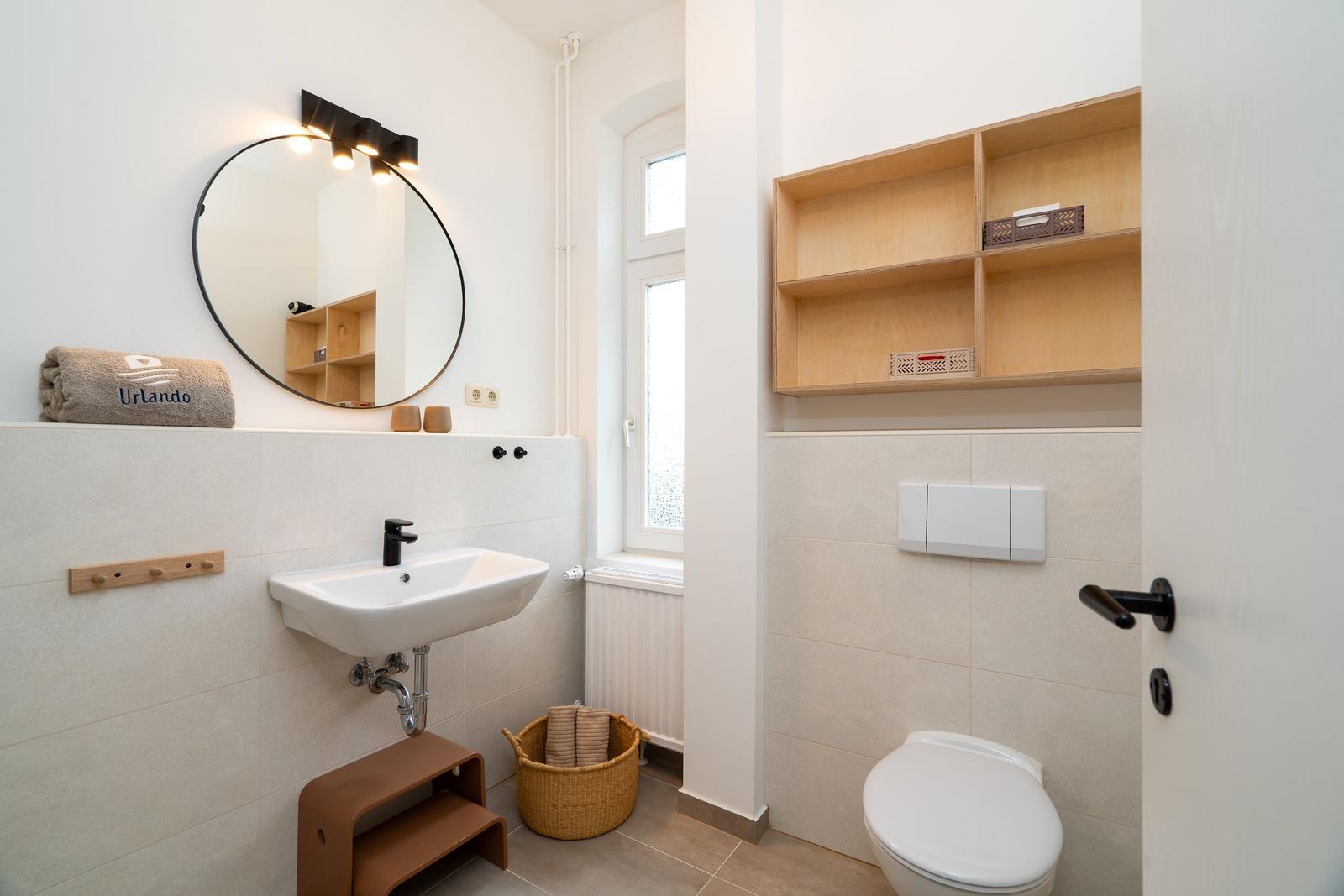 Badezimmer mit Waschbecken, Spiegel, Toilette und Holzregal.