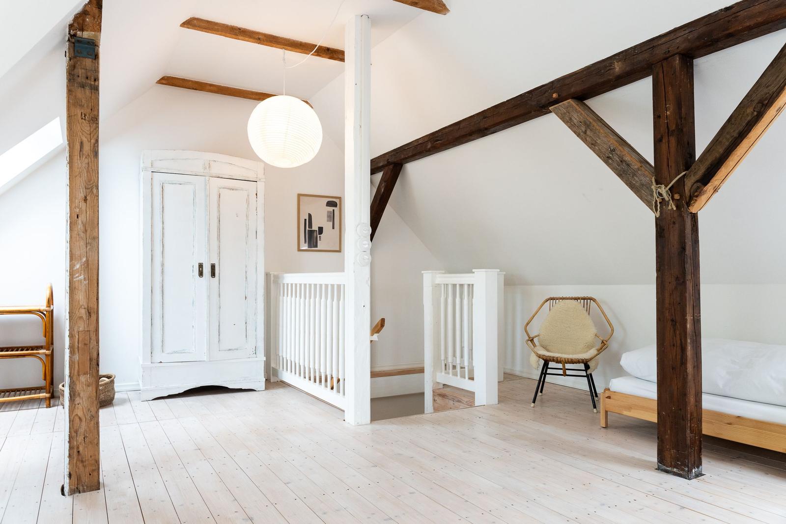 Zimmer mit Holzbalken, weißem Schrank und Bett. Deckenbalken und Boden aus Holz.