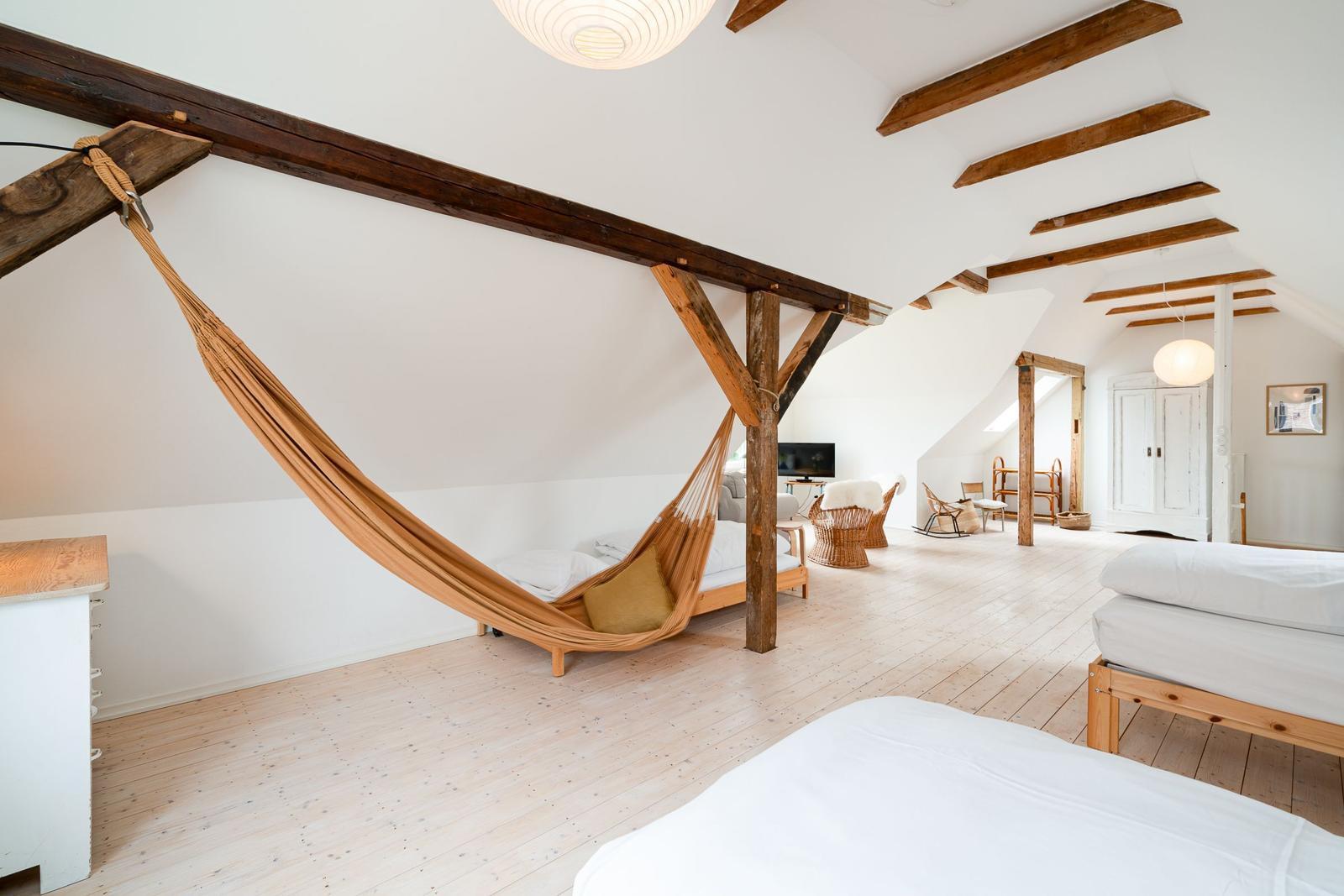Schlafzimmer mit Hängemattensitz, Holzbalken und zwei Betten auf Holzfußboden.