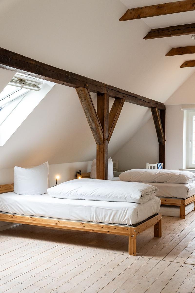 Zwei Betten unter Holzbalken mit Dachfenster und Holzboden.