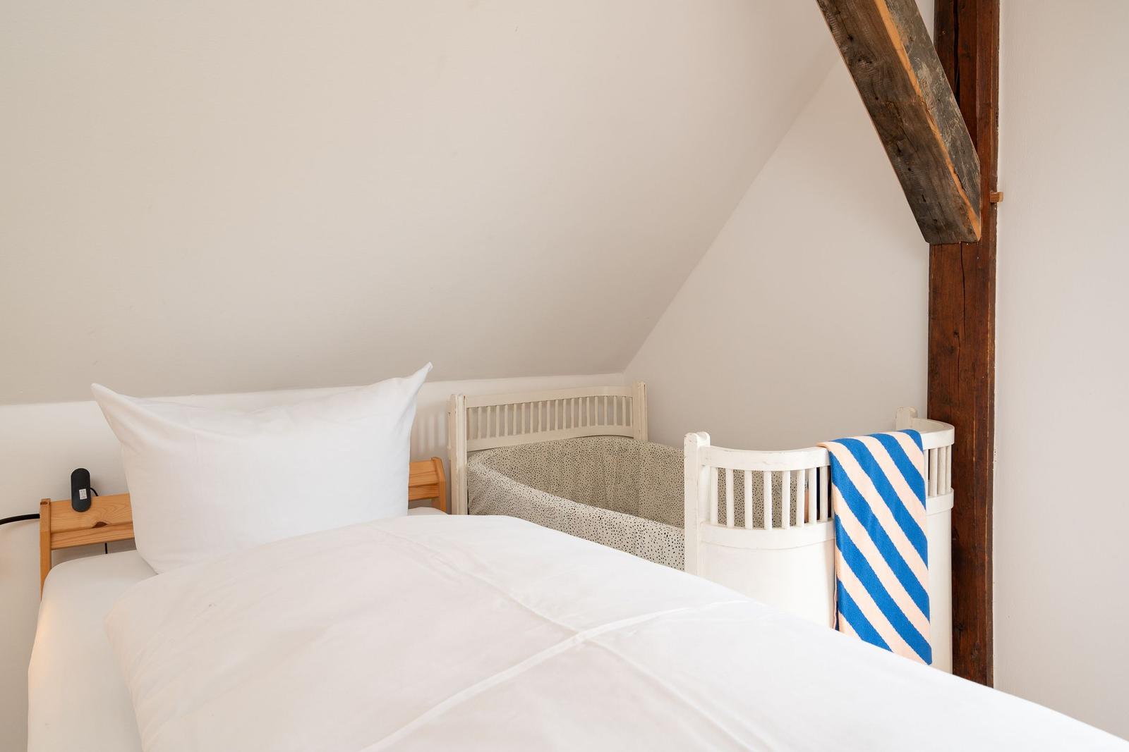 Schlafzimmer mit Bett und Kinderbett unter Holzbalken