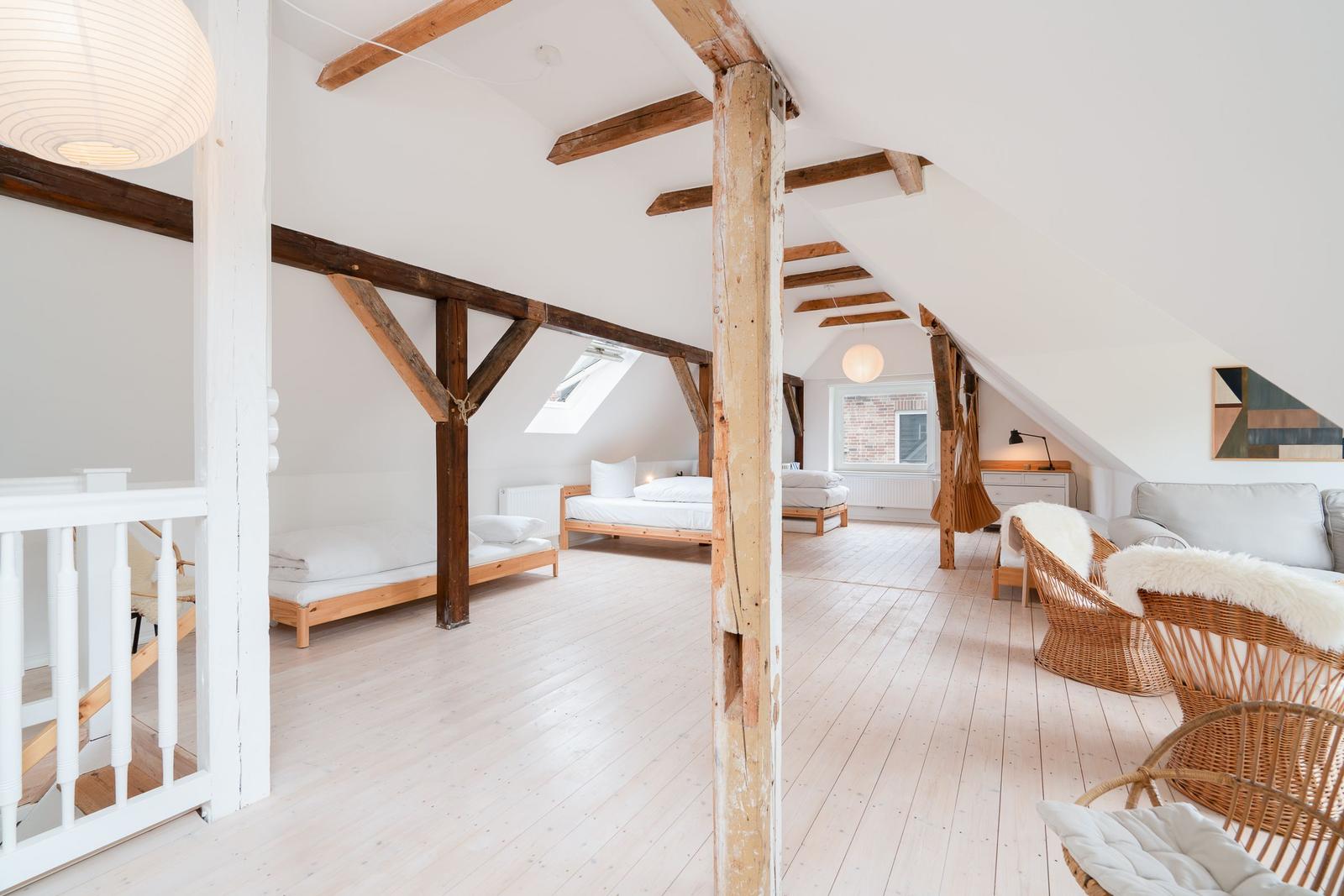 Dachgeschoss mit Holzbalken, zwei Betten und Sitzgelegenheiten.