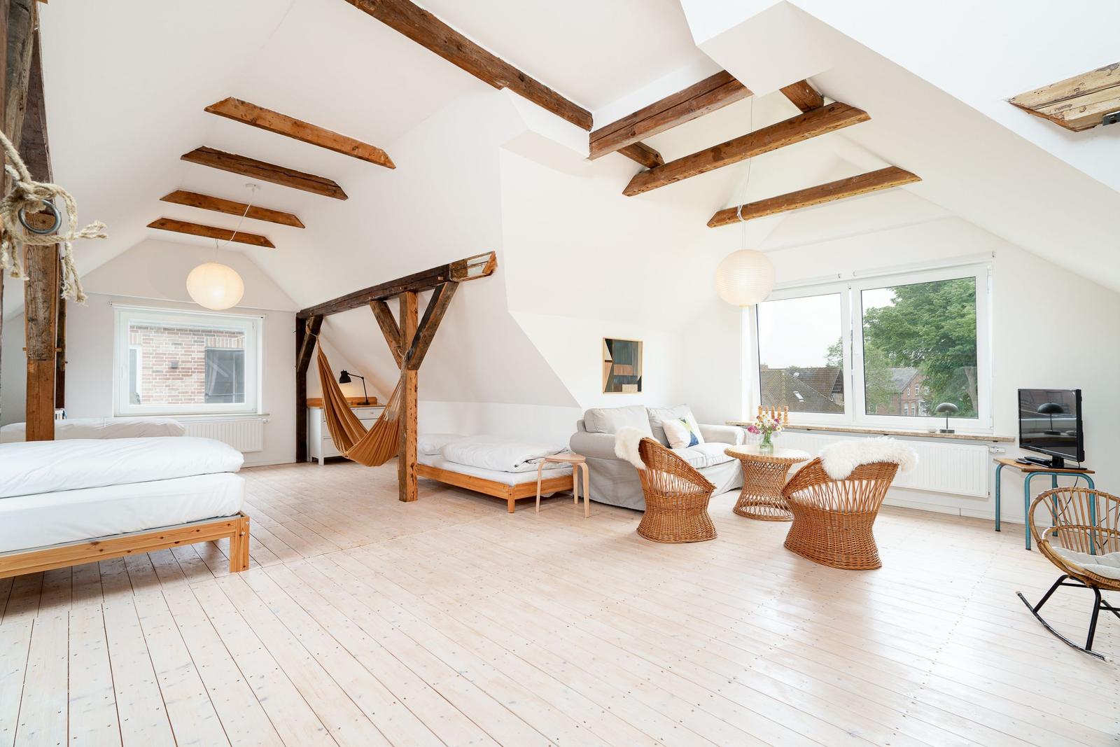 Helle Loft-Wohnung mit Holzbalken, Bett, Sofa und Rattanmöbeln.