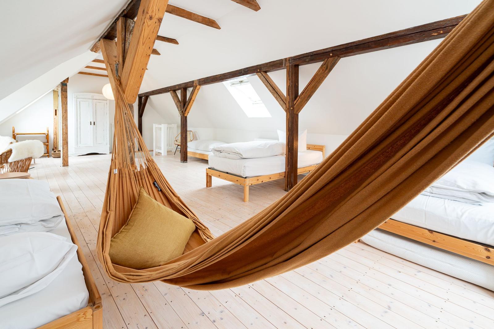 Dachgeschosszimmer mit Hängematte, Holzbalken und mehreren Betten.